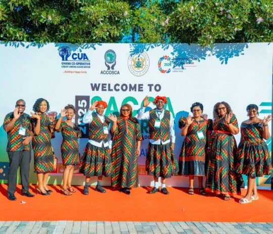 A group of SACCA Congress participants stand together in front of the conference welcome display, wearing traditional attire.